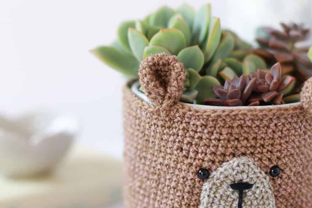 A close up of a crocheted teddy bear planter cover