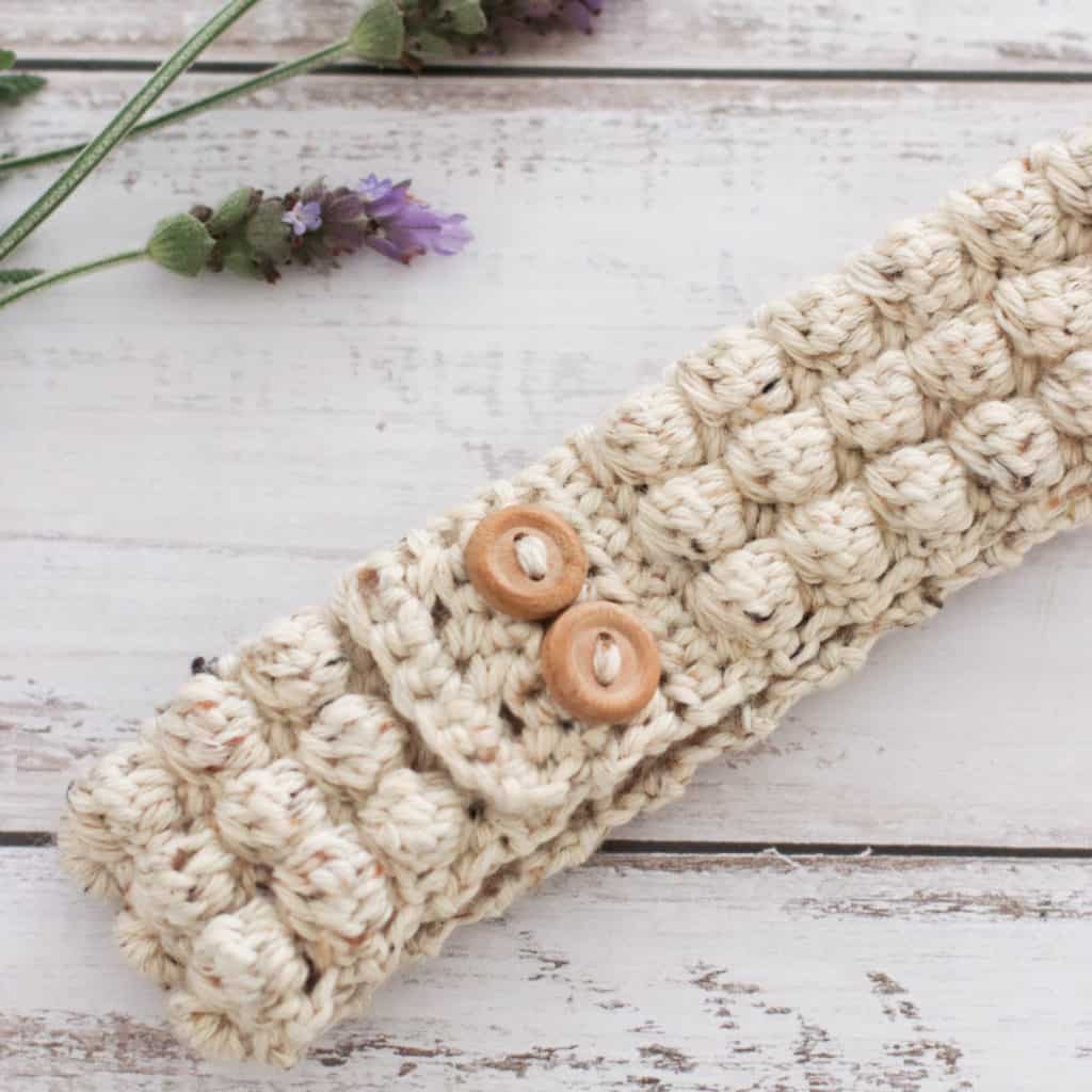 Close up of a crochet headband in natural colors, surrounded by lavender.