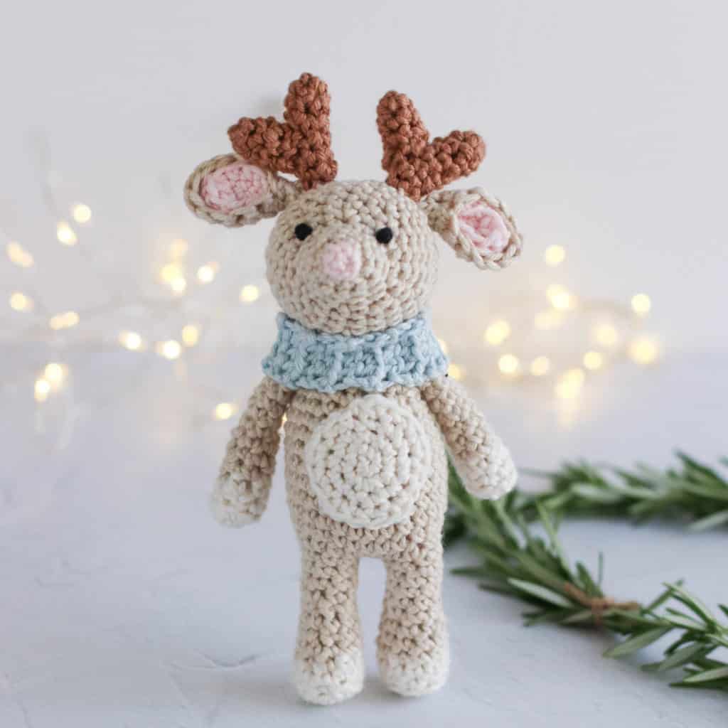 crochet reindeer wearing a scarf with sparkly lights in the background | free crochet reindeer pattern