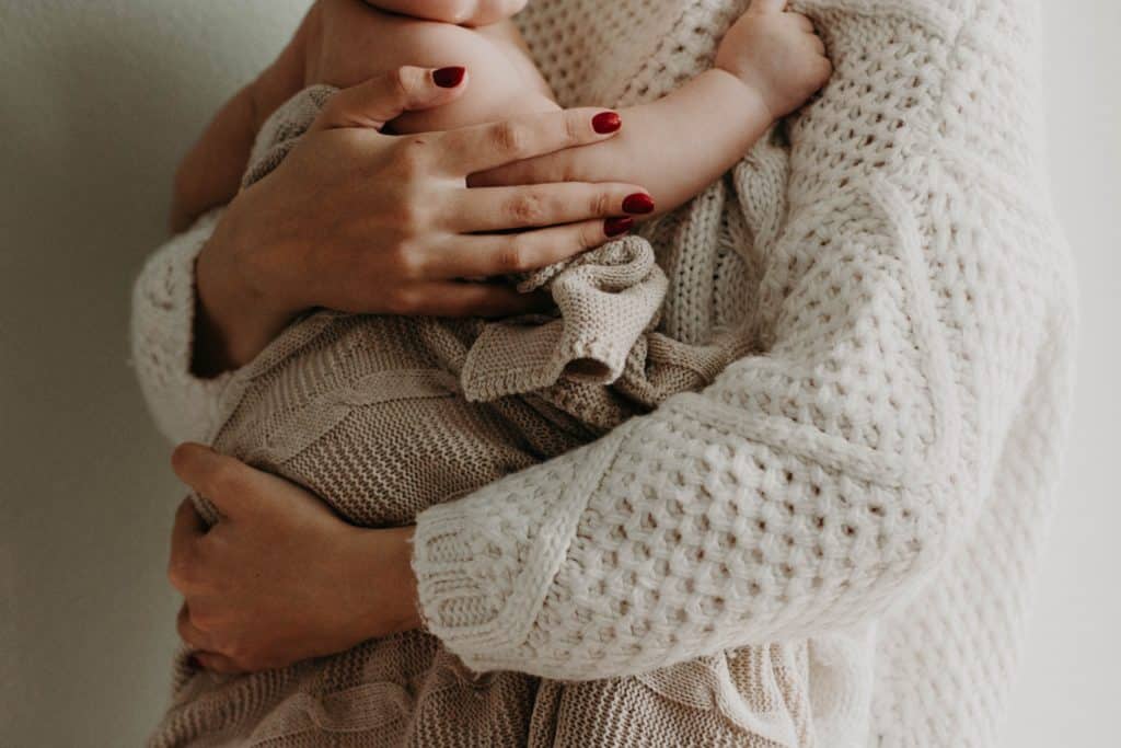 Mother wearing a knitted jersey holding a baby wrapped in a knitted blanket