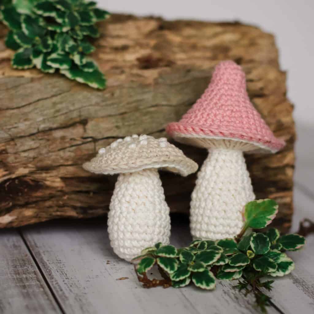 two crochet mushrooms standing side by side in front of some rustic wood