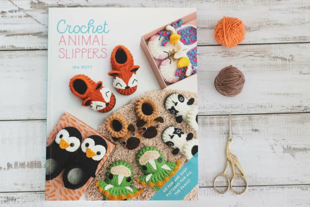 Overhead shot of the book Crochet Animal Slippers by Ira Rott, next to orange and brown yarn