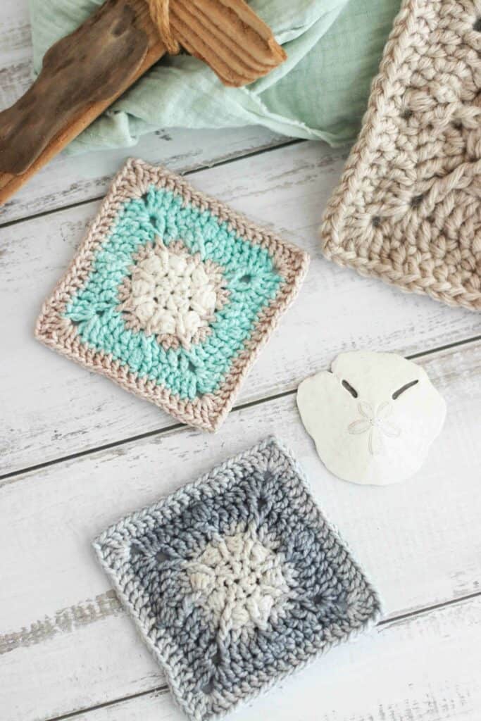 Two crochet granny squares in different ocean colors, next to a sand dollar. 