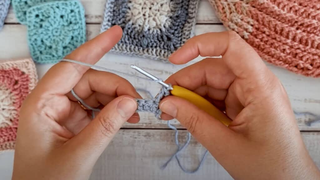 Hands holding purple yarn and a yellow crochet hook, showing people how to crochet a back post double crochet stitch.