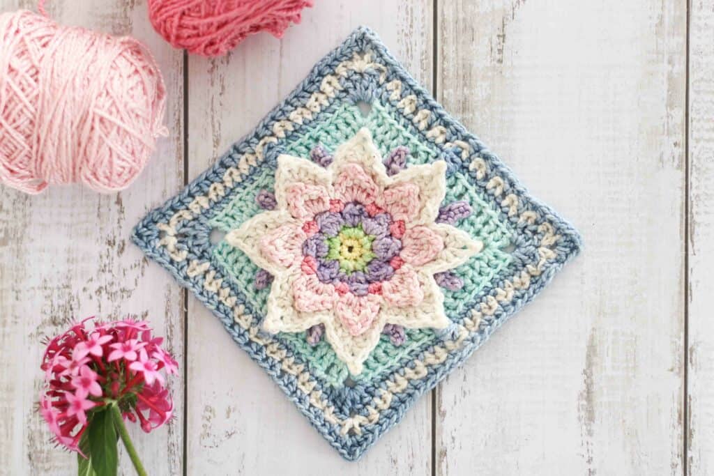 Lotus flower granny square crochet pattern in soft spring colors. This square is surrounded by balls of pink cotton yarn and some delicate pink flowers