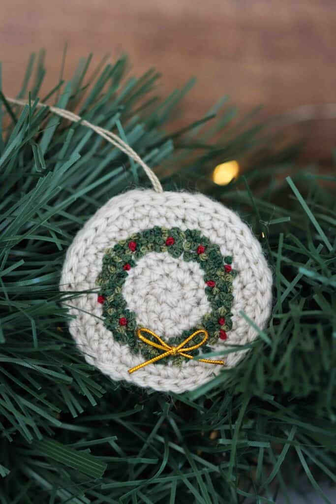 An embroidered crochet Christmas wreath ornament with a small gold bow.