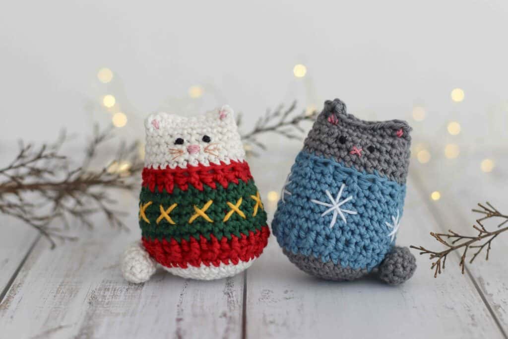 crochet cat pattern, two crocheted kitties wearing festive sweaters. The kitties are surrounded by Christmas lights