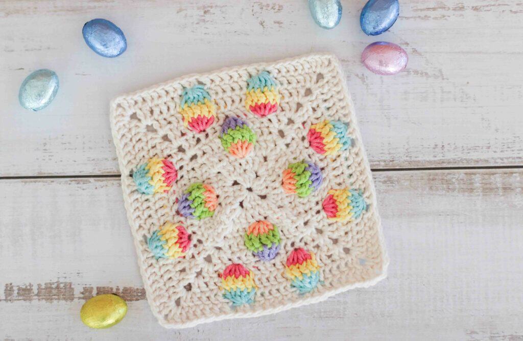 A crochet Easter square surrounded by foil covered chocolate eggs